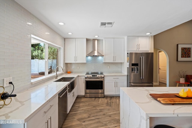 kitchen with wall chimney range hood, sink, white cabinets, appliances with stainless steel finishes, and light stone counters