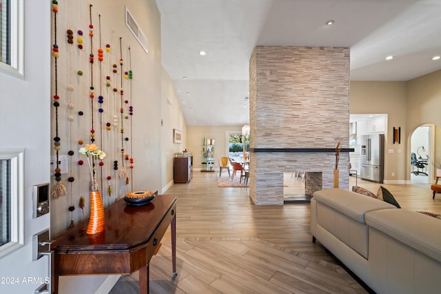 living room with high vaulted ceiling, a fireplace, and light wood-type flooring