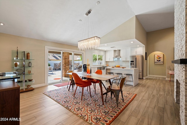 dining room with an inviting chandelier, light hardwood / wood-style flooring, and high vaulted ceiling