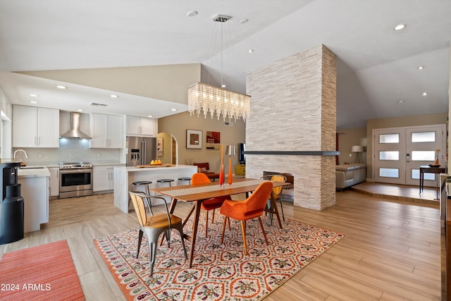 dining area with sink, a chandelier, light hardwood / wood-style flooring, and high vaulted ceiling