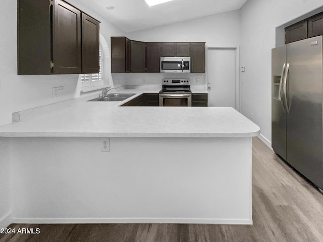 kitchen featuring kitchen peninsula, appliances with stainless steel finishes, dark brown cabinetry, vaulted ceiling, and sink