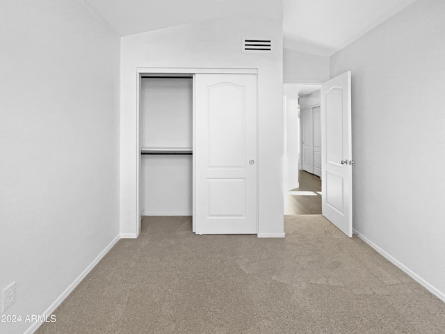 unfurnished bedroom featuring light carpet, a closet, and vaulted ceiling