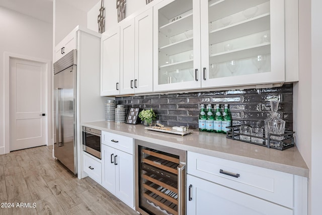 bar with beverage cooler, light wood-type flooring, backsplash, a dry bar, and stainless steel built in refrigerator