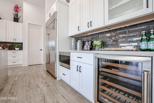 bar featuring built in fridge, beverage cooler, light wood-style floors, decorative backsplash, and a bar