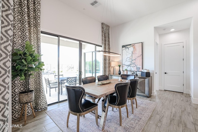 dining area featuring a high ceiling, light wood-type flooring, visible vents, and baseboards