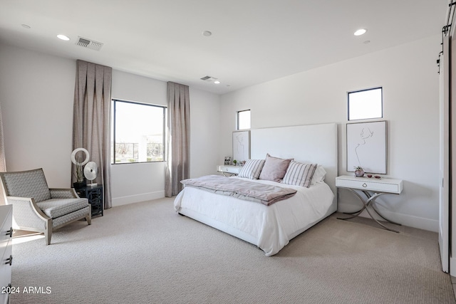 bedroom with light colored carpet, visible vents, recessed lighting, and a barn door