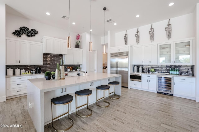 kitchen featuring a breakfast bar area, beverage cooler, white cabinets, light countertops, and stainless steel built in refrigerator