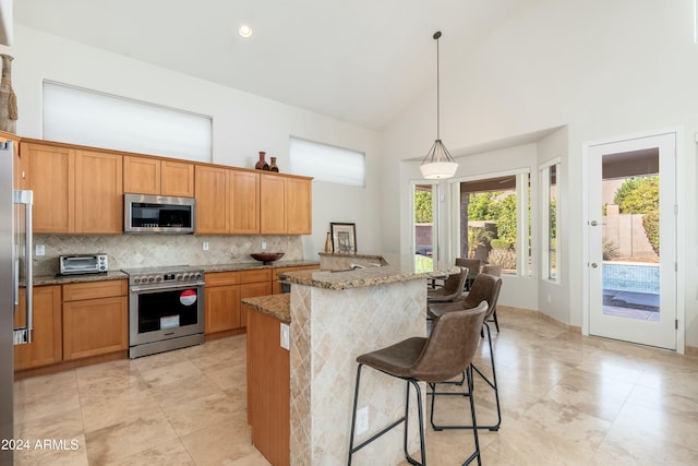 kitchen featuring a kitchen island with sink, high vaulted ceiling, light stone countertops, appliances with stainless steel finishes, and decorative light fixtures