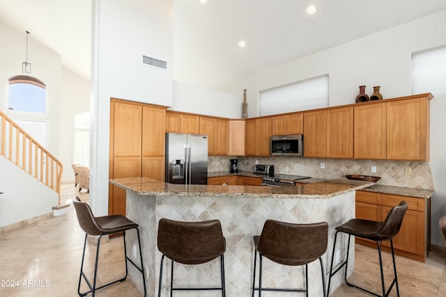 kitchen featuring decorative backsplash, appliances with stainless steel finishes, a towering ceiling, light stone counters, and a breakfast bar area