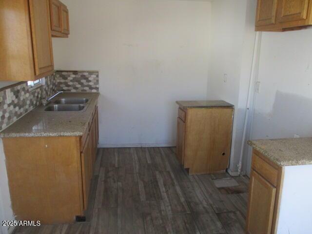 kitchen featuring brown cabinets, backsplash, dark wood-style flooring, and a sink