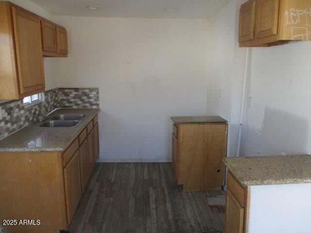 kitchen featuring brown cabinetry, dark wood-type flooring, a sink, light stone countertops, and backsplash