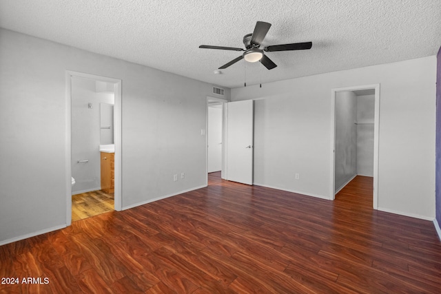 unfurnished bedroom with ensuite bathroom, a spacious closet, ceiling fan, and dark wood-type flooring