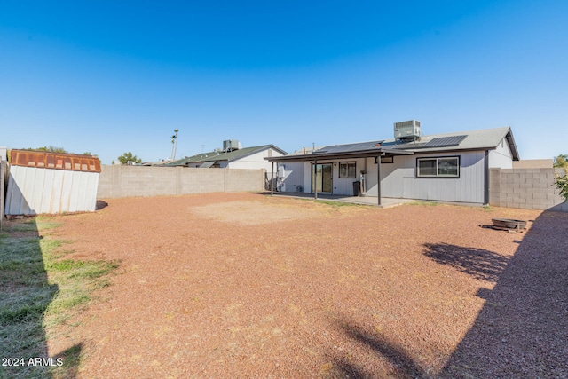 rear view of property with a storage shed, a patio area, cooling unit, and solar panels