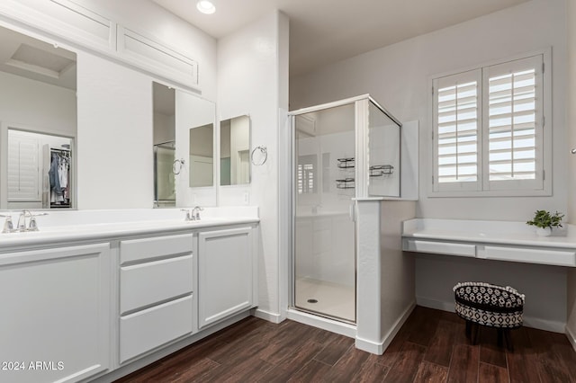 bathroom with double vanity, a stall shower, a sink, wood finished floors, and baseboards