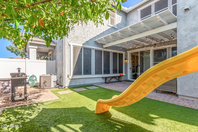 view of jungle gym with a lawn, a patio area, central AC, fence, and a pergola