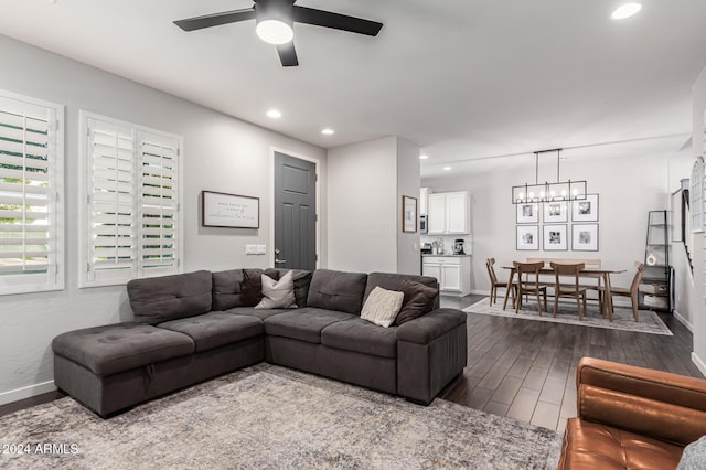 living area featuring dark wood-type flooring, baseboards, and ceiling fan with notable chandelier