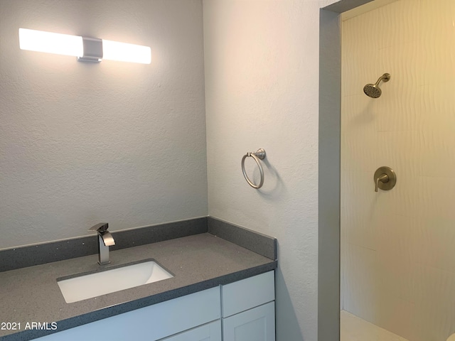 full bathroom with a textured wall, tiled shower, and vanity