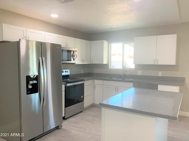 kitchen with white cabinetry, stainless steel appliances, a sink, and a center island