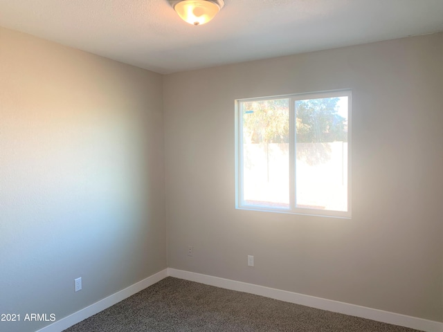 empty room featuring a wealth of natural light, dark carpet, and baseboards