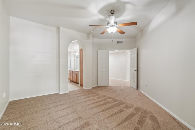 spare room featuring light colored carpet, arched walkways, visible vents, and baseboards