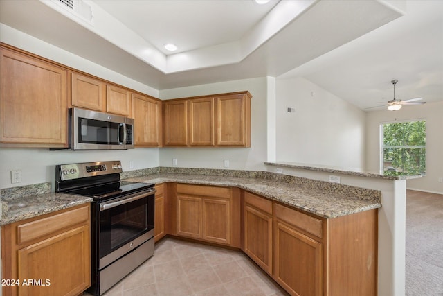 kitchen with appliances with stainless steel finishes, a raised ceiling, a peninsula, and light stone countertops