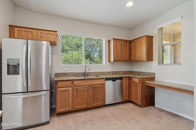 kitchen with a sink, light stone countertops, appliances with stainless steel finishes, and brown cabinets