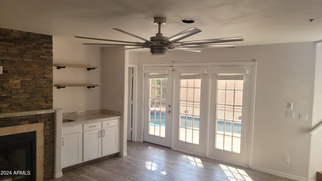 interior space with ceiling fan, light hardwood / wood-style floors, a stone fireplace, and a healthy amount of sunlight