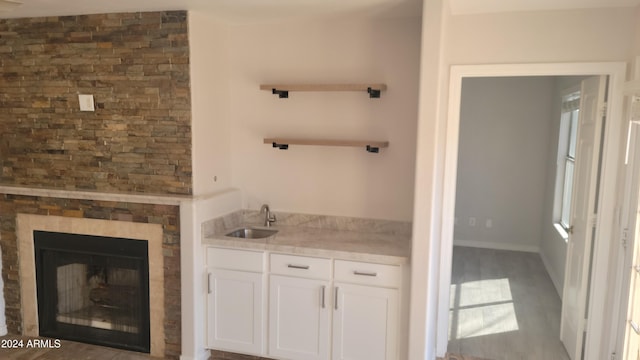 bar with white cabinets, a large fireplace, sink, and dark wood-type flooring