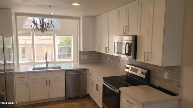 kitchen with dark tile patterned floors, white cabinetry, appliances with stainless steel finishes, an inviting chandelier, and sink