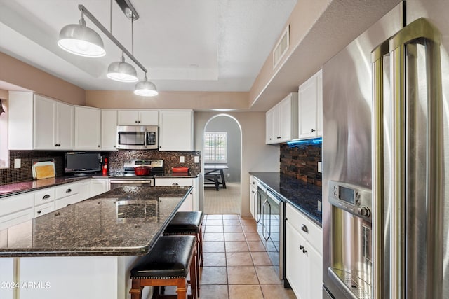 kitchen featuring tasteful backsplash, white cabinets, a kitchen island, appliances with stainless steel finishes, and decorative light fixtures