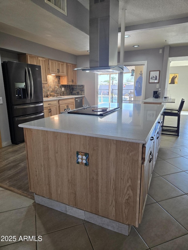 kitchen featuring island exhaust hood, black appliances, light tile patterned flooring, light brown cabinetry, and decorative backsplash