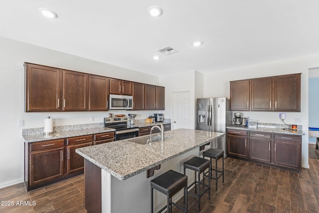 kitchen featuring a breakfast bar, sink, a kitchen island with sink, stainless steel appliances, and light stone countertops