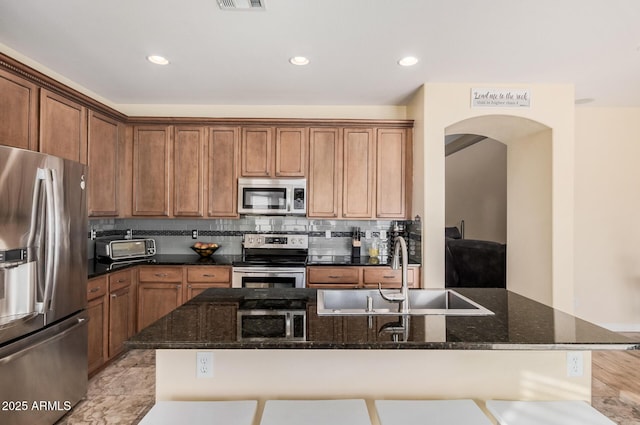 kitchen featuring a breakfast bar area, stainless steel appliances, dark stone counters, backsplash, and sink