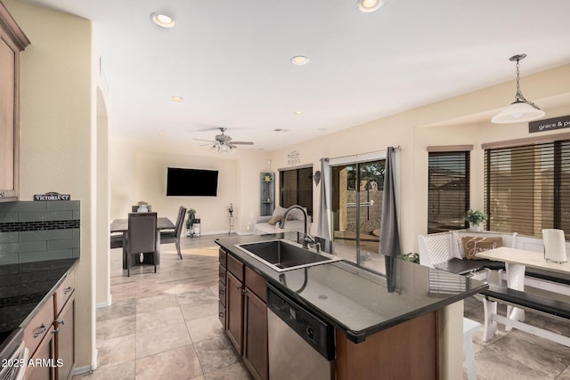 kitchen with a center island with sink, hanging light fixtures, dishwasher, sink, and dark stone countertops