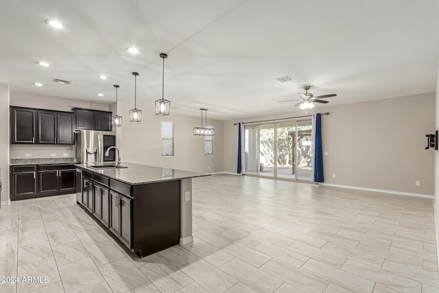 kitchen with sink, an island with sink, stainless steel fridge, ceiling fan, and decorative light fixtures