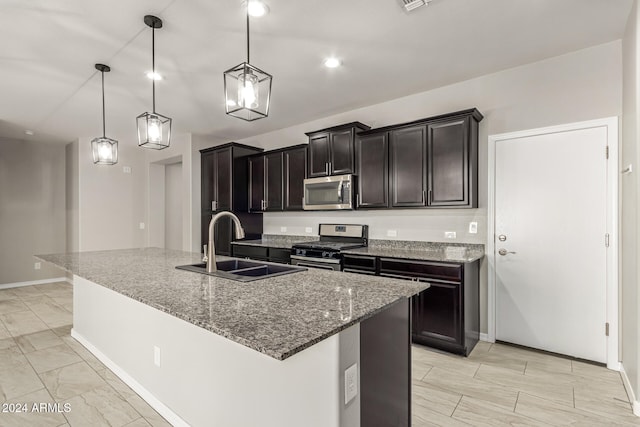 kitchen featuring appliances with stainless steel finishes, a kitchen island with sink, dark stone counters, sink, and decorative light fixtures