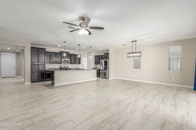 kitchen with dark brown cabinets, ceiling fan, appliances with stainless steel finishes, a kitchen island with sink, and decorative light fixtures