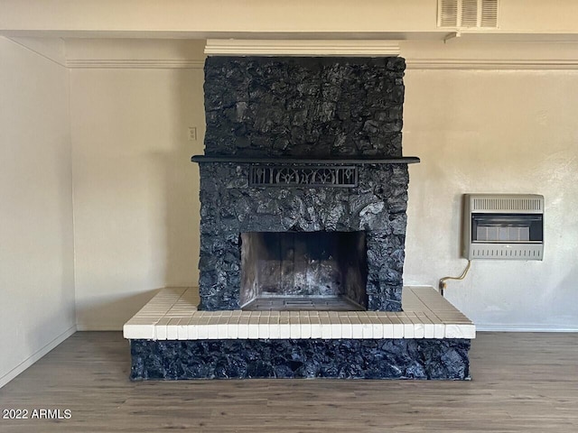 details featuring heating unit, visible vents, wood finished floors, and a large fireplace