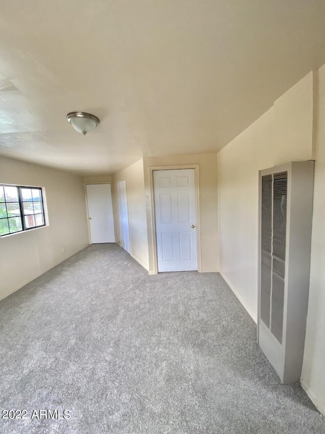 unfurnished bedroom with a heating unit and carpet flooring