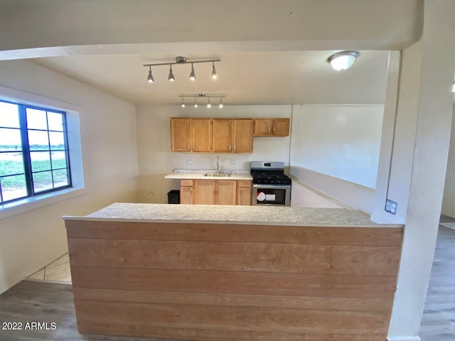 kitchen featuring kitchen peninsula, rail lighting, sink, stainless steel gas range, and hardwood / wood-style flooring