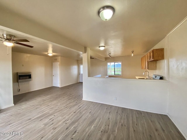 unfurnished living room with a sink, heating unit, wood finished floors, and ceiling fan