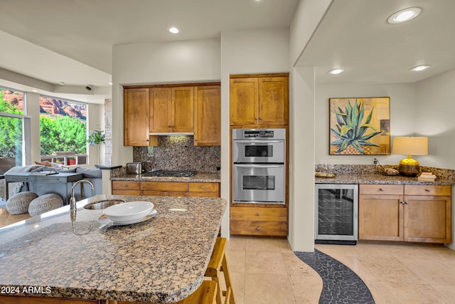 kitchen with dark stone counters, a sink, brown cabinets, stainless steel appliances, and beverage cooler