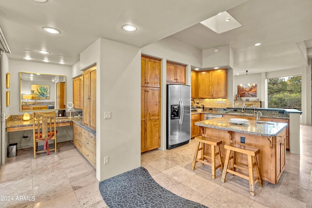 kitchen with a breakfast bar area, a sink, stainless steel refrigerator with ice dispenser, and a peninsula