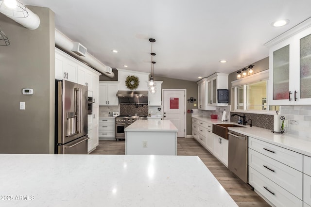 kitchen with vaulted ceiling, high end appliances, sink, decorative light fixtures, and a kitchen island