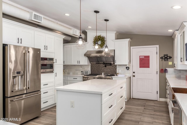 kitchen with white cabinetry, a kitchen island, wall chimney exhaust hood, and appliances with stainless steel finishes