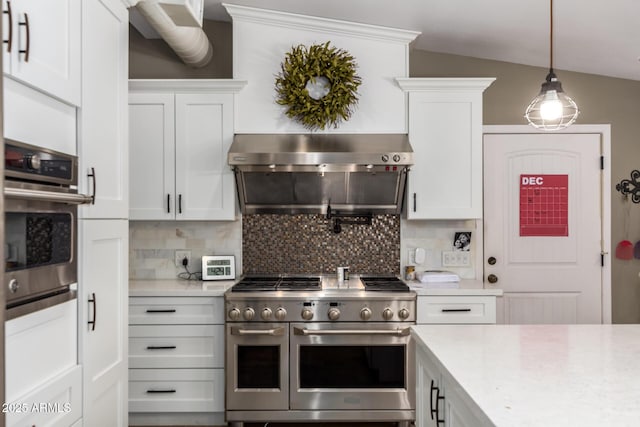 kitchen with white cabinetry, stainless steel appliances, wall chimney range hood, and decorative light fixtures