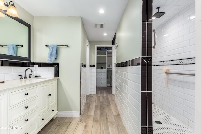 bathroom featuring tiled shower, hardwood / wood-style floors, vanity, and tile walls