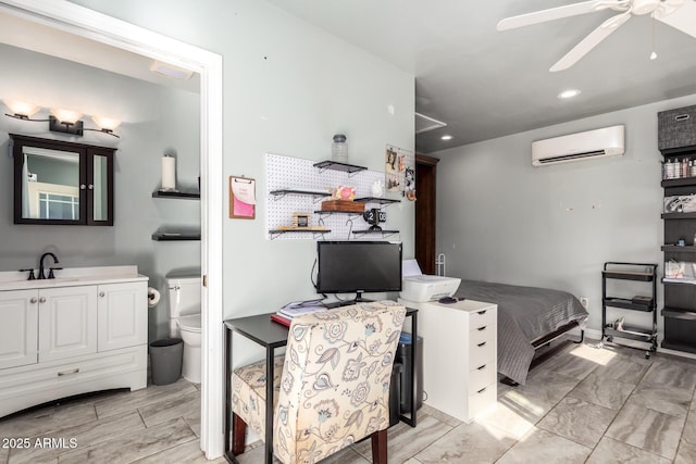 bedroom featuring a wall unit AC, ensuite bath, ceiling fan, and sink