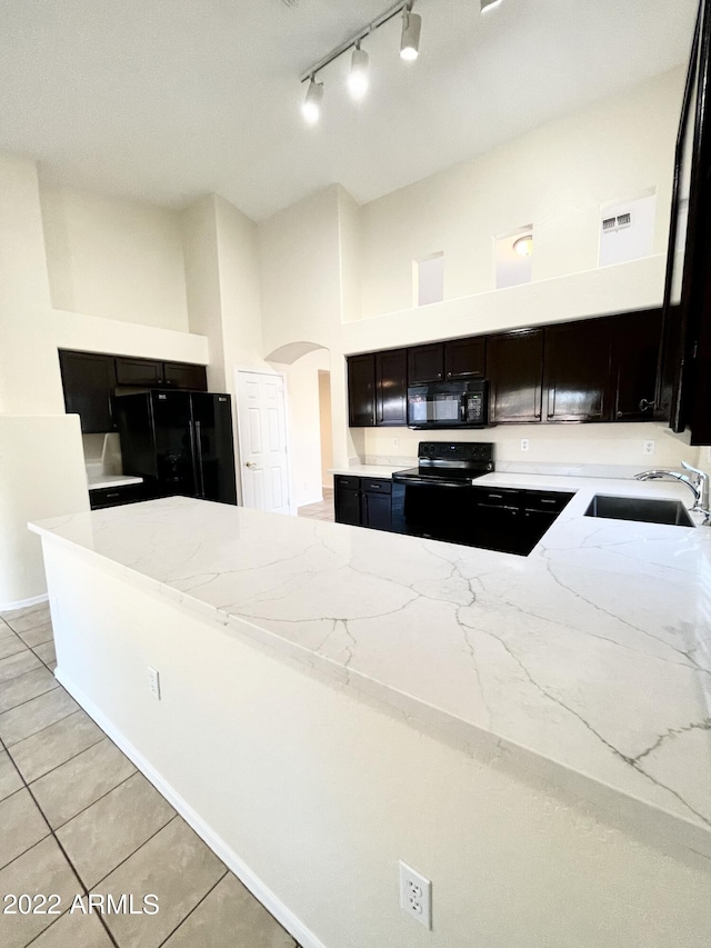 kitchen with sink, a high ceiling, light tile patterned floors, light stone counters, and black appliances