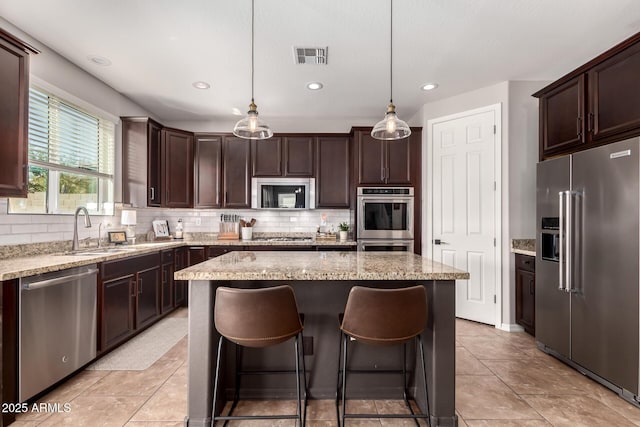 kitchen featuring visible vents, decorative backsplash, a kitchen island, stainless steel appliances, and a sink